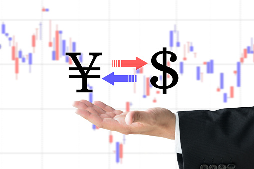 Business man's hand raising Japanese yen and dollar marks on chart background