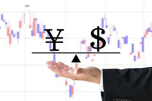 Business man's hand raising Japanese yen and dollar marks with scale on chart background
