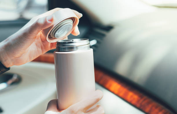 Close up of woman's hands holding reusable insulated water bottle in car Close up of woman's hands holding reusable insulated water bottle and opening the lid in car in bright sunlight flask stock pictures, royalty-free photos & images