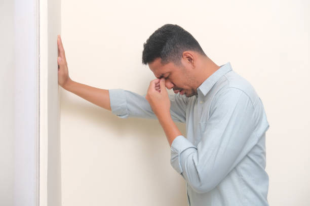 vue latérale d’un homme asiatique adulte montrant une expression triste avec une main tenant sur le mur - pusing photos et images de collection