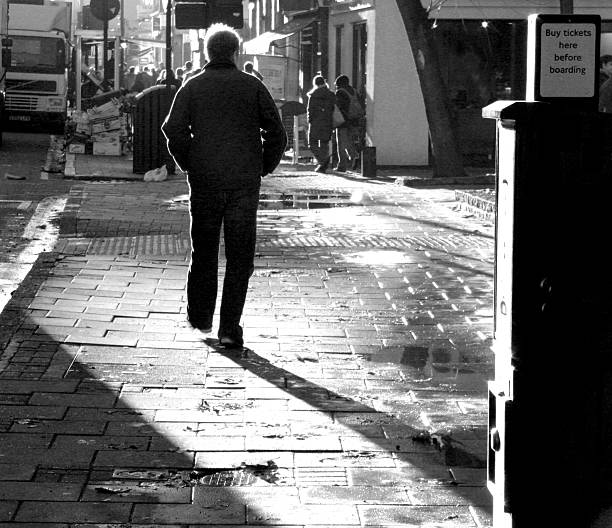 Black and white of a man with his hands in his pockets walking down Tottenham Court Road in London, England in strong morning sunlight. Taken on 19 November 2004 by Stacy Munn.