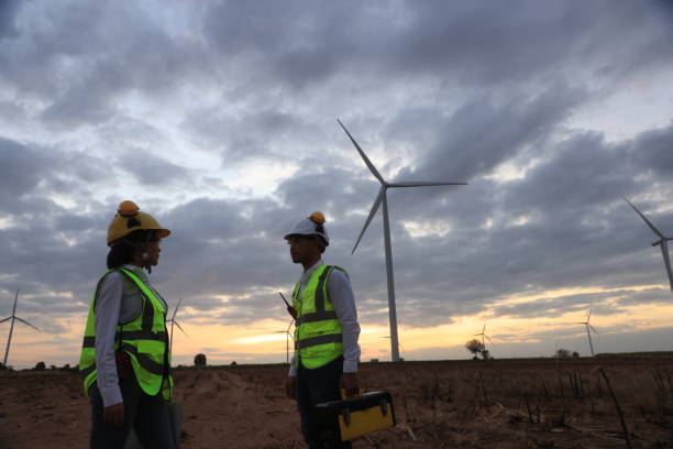 istock Young engineer discussion about wind turbine project at wind turbine farm. Two engineers discussed the plan for the maintenance of wind turbines 1392676765