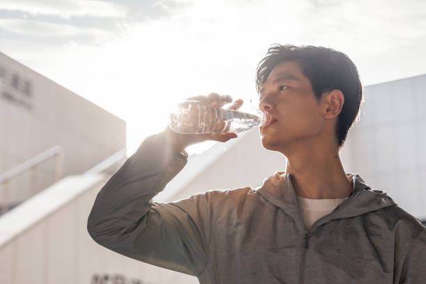 giovani uomini asiatici che bevono acqua alla luce del sole dopo l'esercizio - drinking men water bottle foto e immagini stock