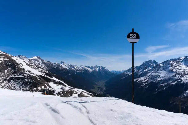Landscape shot in saint anton at arlberg in austrian alps with snow and a black piste sign showing the beginning of a difficult steep slope against partly cloudy blue sky