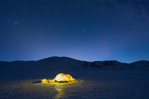 A yellow tent pitched on a frozen lake under the stars.