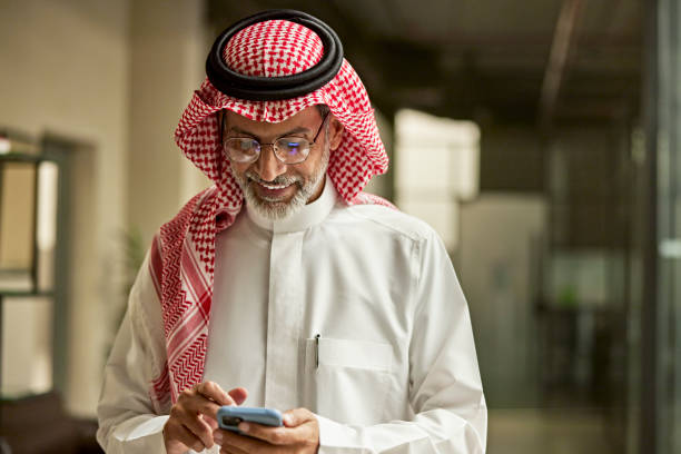 sonriente hombre de negocios saudí revisando el teléfono inteligente en la oficina - agal fotografías e imágenes de stock