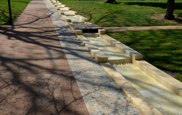 istock promenade in the park, an artificial stream in a sunken gutter on the slope. water flows through the pump up and down the stairs and waterfalls cascade of stairs. beige pond and wooden bridge 1392685104