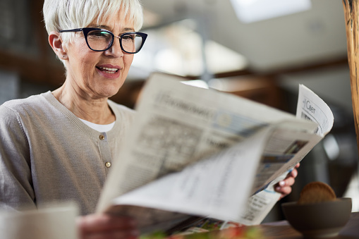 Happy mature woman enjoying while reading newspapers at home.