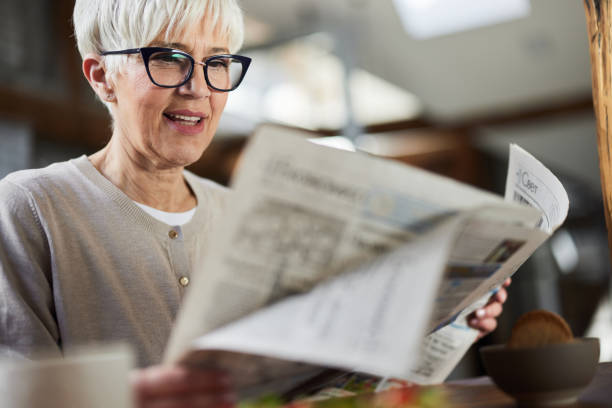 счастливая пожилая женщина, читающая газеты дома. - newspaper glasses the media reading стоковые фото и изображения