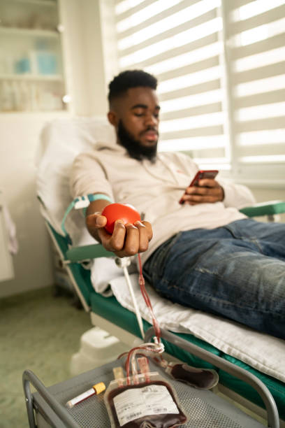 Blood doner at the donation clinic A male blood doner looking at his mobile during blood donation at the bright modern blood donation clinic blood bank stock pictures, royalty-free photos & images