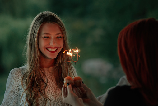 Redhead friend holding sparkler for her blonde friend , which is celebrating her birthday
