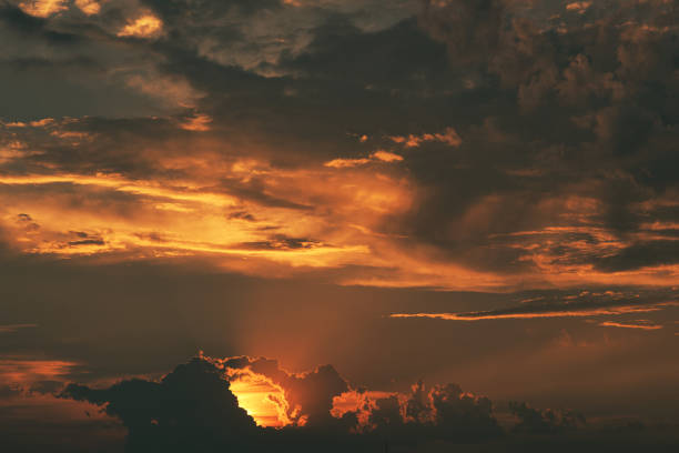 Sky at sunrise or sunset. White clouds lit by bright orange yellow sun on clear blue sky