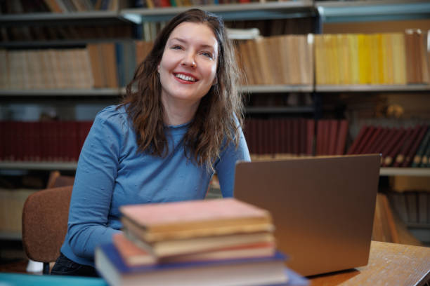 istock Female post-grad using laptop at the desk in the library and smiling 1392692303