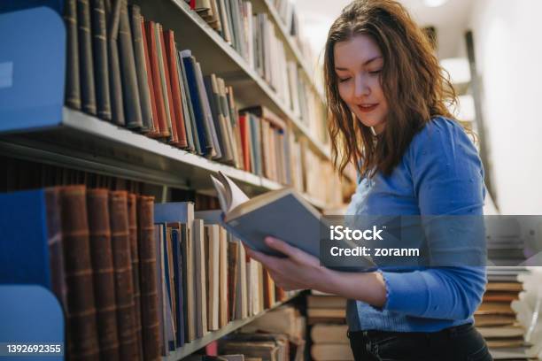 Postgrad Holding A Book With Study Material By The University Library Shelves Stock Photo - Download Image Now