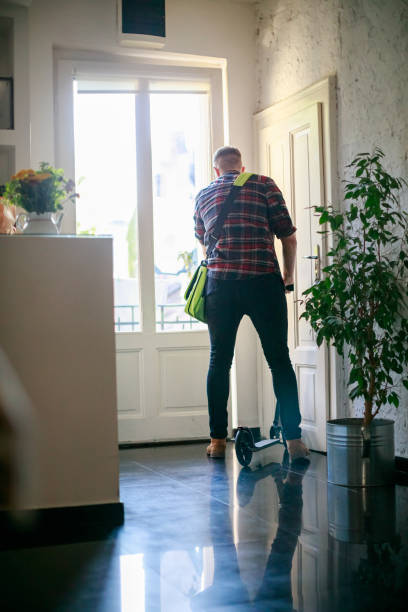 istock Young man with bag over shoulder going out on push scooter 1392694562