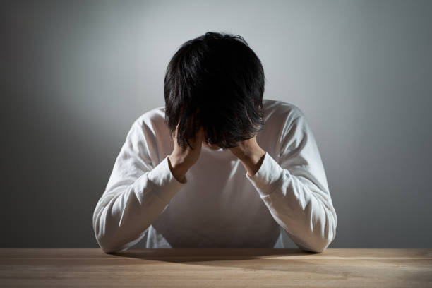 暗い部屋でうつ状態のアジア人男性 - 悔しい ストックフォトと画像