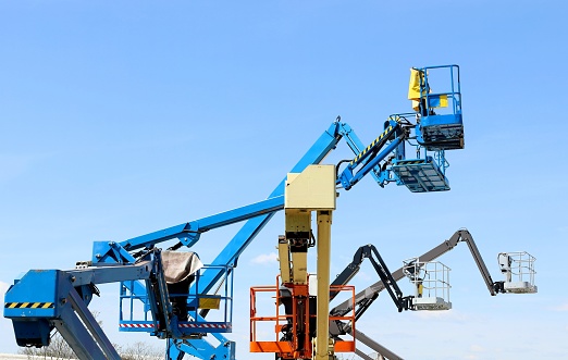 Group of aerial working platforms of cherry picker against blue sky. Back and side view.