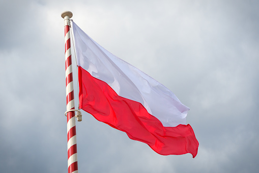 The Polish flag flutters on the mast against the cloudy sky. Wind, clouds and flag