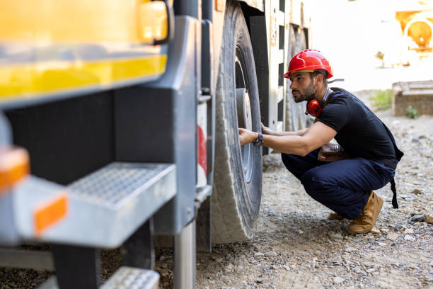 A Mechanic Worker is Checking the Tire of a Truck. A Construction Worker with a Protective Helmet is Checking the Tire of a Truck at the Construction Site. crane truck stock pictures, royalty-free photos & images