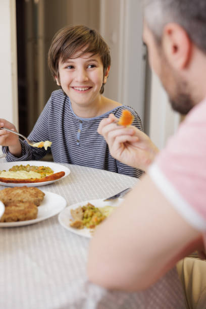 istock Happy boy sitting at the dining table, looking at his father and having lunch 1392698665