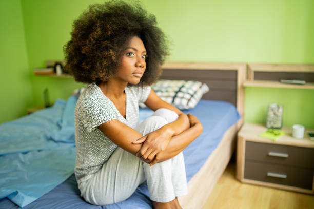 istock A sad woman sitting on a bed hugging her knees 1392698682