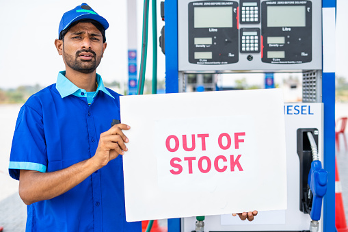 Worker at petrol or gas filling sation showing out of stock notice sign board - concept of economy and fuel crisis shortage.