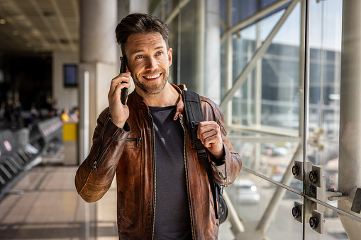 A portrait of a handsome modern man who is in an airport building, using a mobile phone after getting off a plane