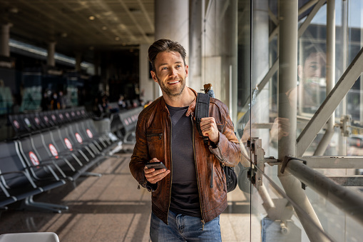 A portrait of a handsome modern man who is in an airport building, using a mobile phone after getting off a plane