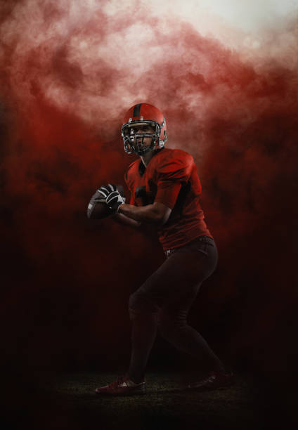 Red sky. Creative portrait of young man, american football player at stadium in motion on smoked background. Sport, challenge, goals, activity, sportlife concept. Red sky. Portrait of young man, american football player at stadium in motion on smoked background. Sport, challenge, goals, activity, sportlife concept. Poster, flyer for ad, design. american football player stock pictures, royalty-free photos & images