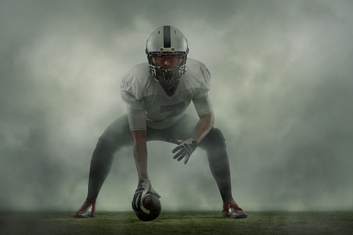 Linebacker. Creative portrait of young man, american football player at stadium in motion on smoked background. Sport, challenge, goals, activity, sportlife concept. Poster, flyer for ad, design.