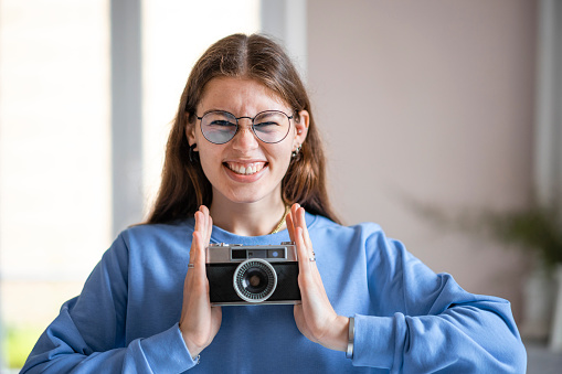 Front view medium shot of a woman smiling pulling a face while holding a retro digital camera. She is in Toulouse.