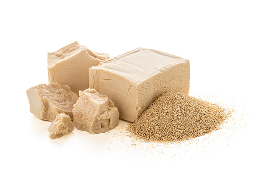 Front view of a cube of fresh yeast next to a heap of dried yeast isolated on white background