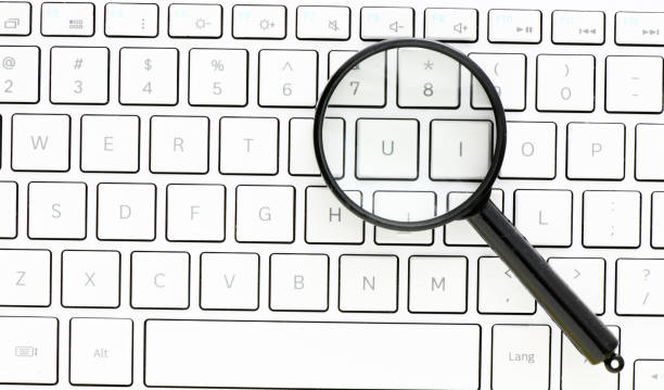 istock Black magnifying glass on the background of a white computer keyboard. 1392713180
