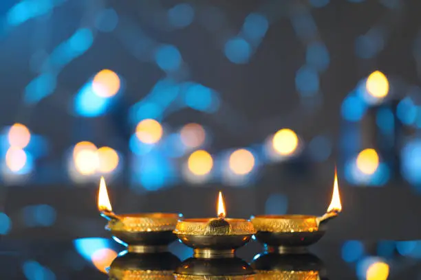 Photo of Lit diyas on table against blurred lights. Diwali lamps