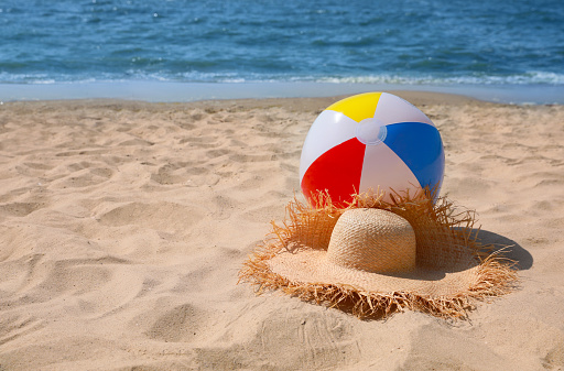 Straw hat and beach ball near sea. Space for text