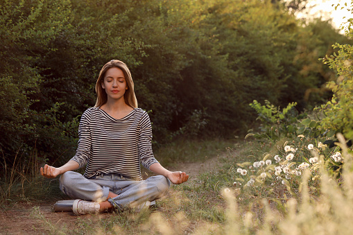 Young woman meditating on green grass outdoors, space for text