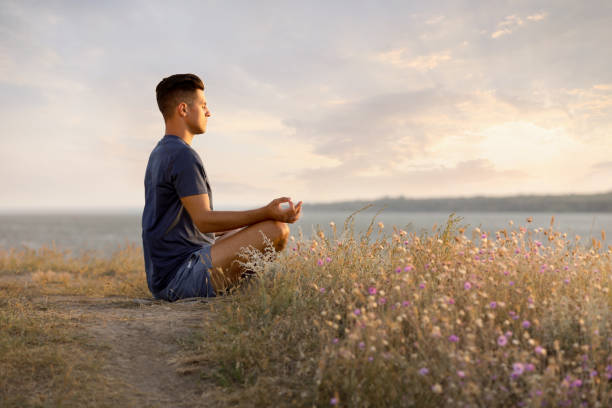 Man meditating near river on sunny day, space for text
