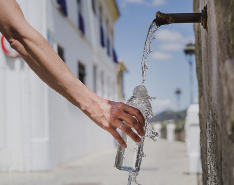 foto de una mano sosteniendo una botella de vidrio llenándola con agua natural de una fuente photo