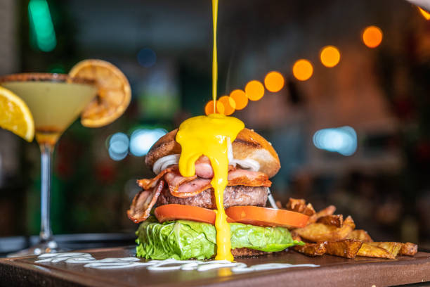 Close-up of an hamburger with melted cheese pouring on it inside a nightclub restaurant Close-up of an hamburger with melted cheese pouring on it and a cocktail inside a nightclub restaurant spanish hamburger stock pictures, royalty-free photos & images