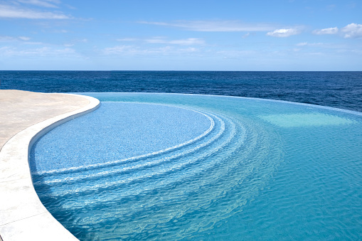Sea water pool with stairs for relaxing, sea views. Blue clear water surface in swimming pool. Summer Vacation and rest concept. Ripples on water. Pattern of bottom made of mosaic ceramic blue tiles.
