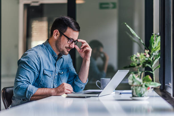 istock Confident businessman wearing eyeglasses using laptop at table in home office 1392719978