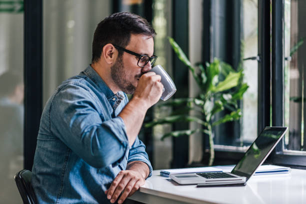 istock Young freelancer drinking coffee while working on laptop at table in home office 1392719981