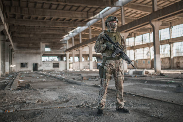 istock Confident soldier with rifle in camouflage uniform in war zone 1392720047