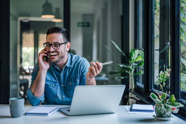 istock Smiling distracted businessman talking on phone while using laptop at home 1392720061