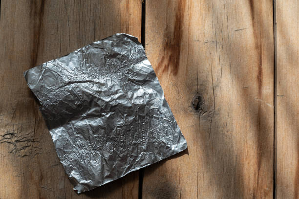istock Rectangular aluminum candy wrapper against a wooden background. Rough, cracked boards. Natural lighting. 1392720442