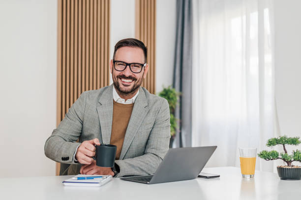 istock Confident smiling professional having coffee while working on laptop at desk 1392720516