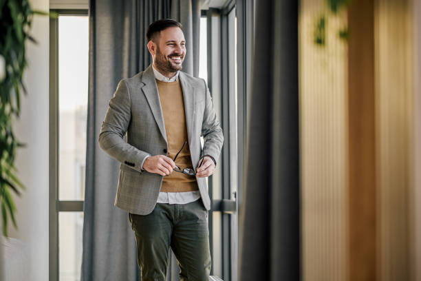 Successful happy entrepreneur looking through window while standing at office