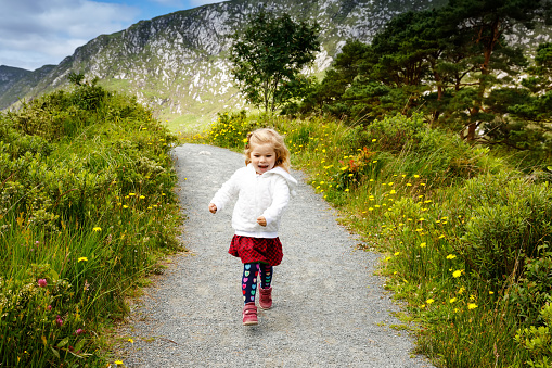 Cute little happy toddler girl running on nature path in Glenveagh national park in Ireland. Smiling and laughing baby child having fun spending family vacations in nature. Traveling with small kids.