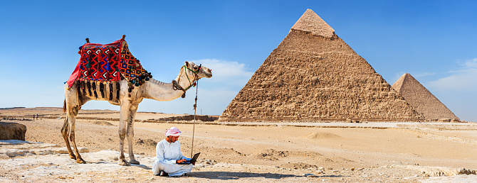 Egypt, Cairo, asian group tourists riding camel with Great Pyramid of Giza in background