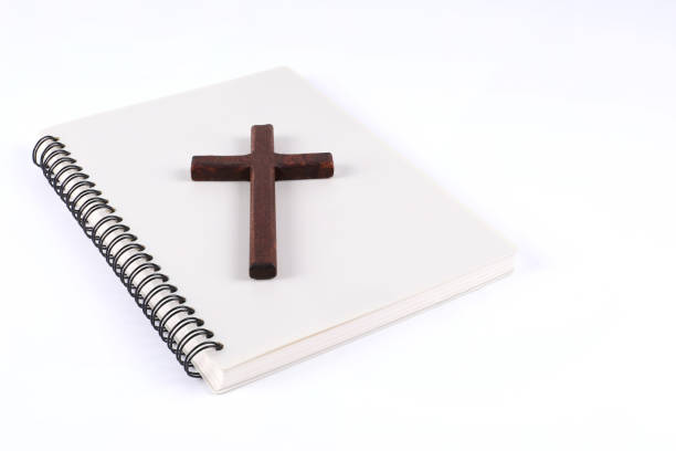 istock Wooden christian cross placed on a book with white background with writing area 1392727310